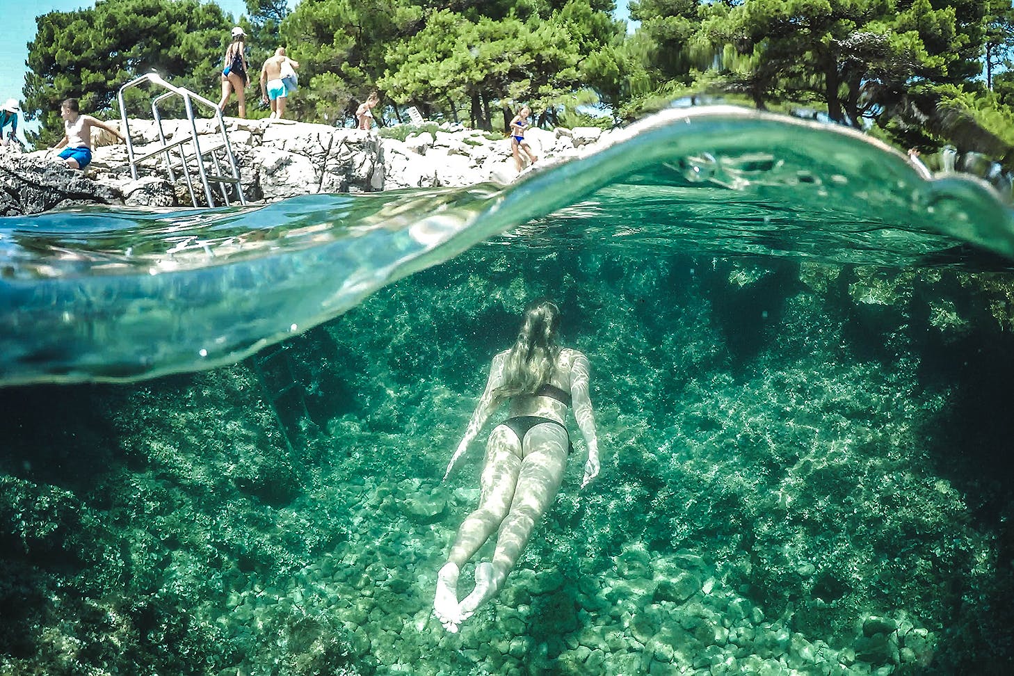 A woman swims through green water to the land above.
